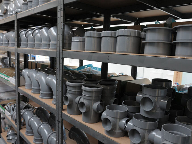 Grey PVS elbows and fittings on a shelf in a plumbing supply warehouse